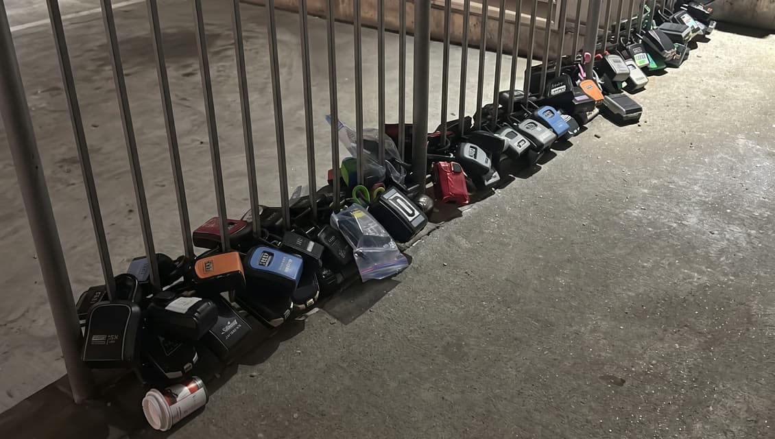 Dozens of lockboxes heaped along a garage railing, a discarded coffee cup among them